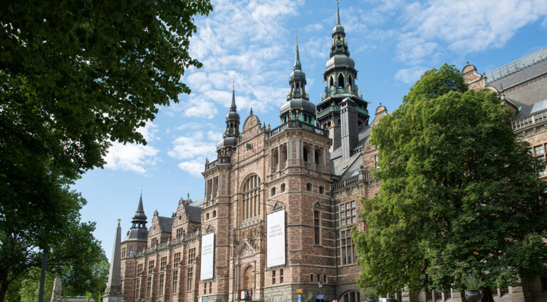 Stort museibyggnad med torn, omgiven av grönskande träd.