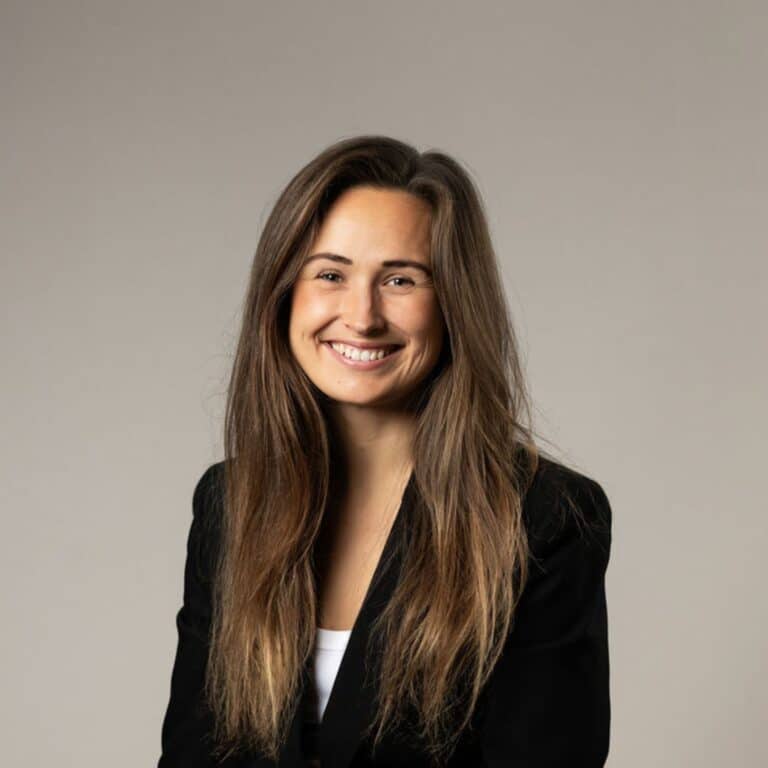 En glad kvinna med långt hår och som bär en vit skjorta och svart kavaj.