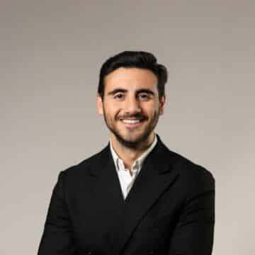 Glad kille med svart hår och bär en vit skjorta och svart kavaj.