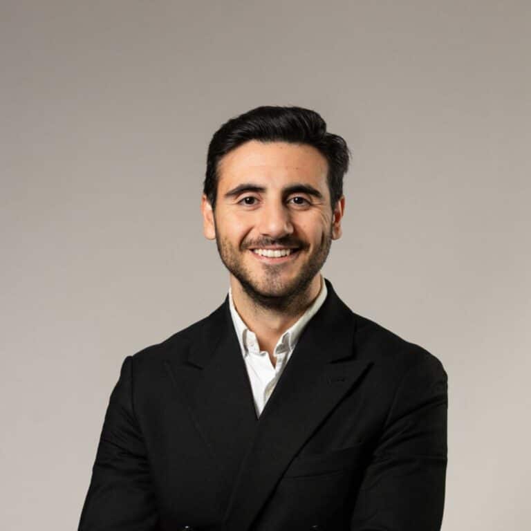 Glad kille med svart hår och bär en vit skjorta och svart kavaj.