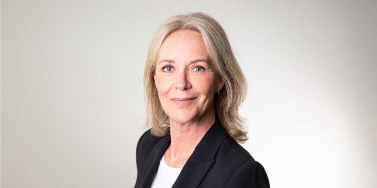 Kvinna i kostymjacka ler framför ljus bakgrund.