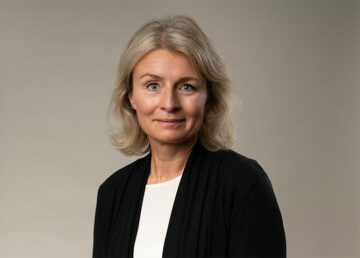 Kvinna med grått hår, tittar framåt mot lugn bakgrund.