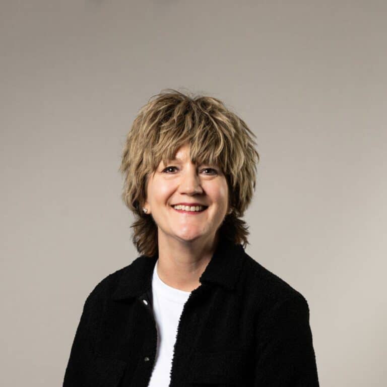 En glad kvinna med kort hår som ler mot kameran