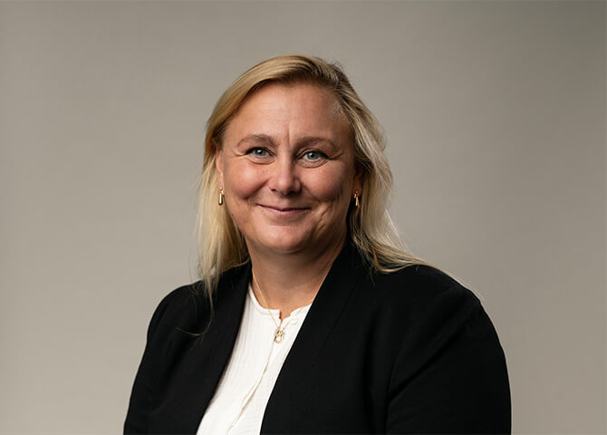 Kvinna ler, klädd i formell dräkt, neutral bakgrund.