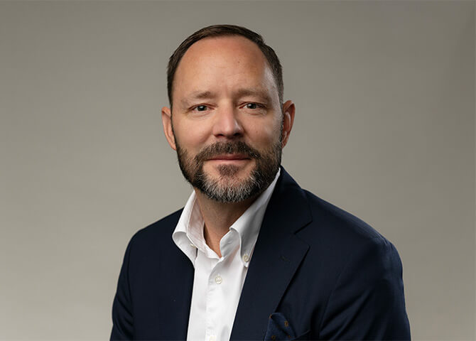 Man sitter i kostym och tittar mot kameran.