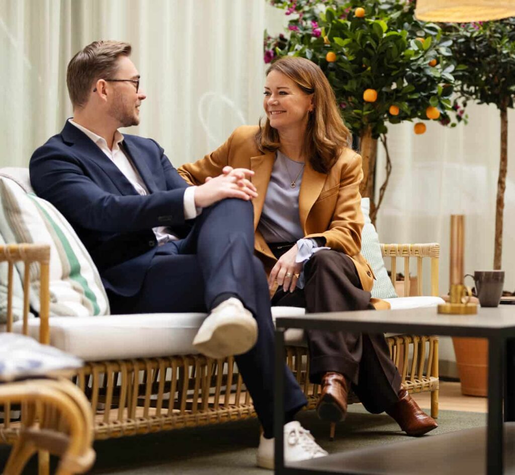 Två personer samtalar på en soffa i en trädgård.