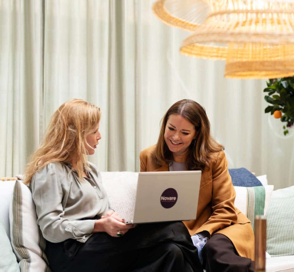Två kvinnor samtalar, tittar på laptop med texten "Novare".