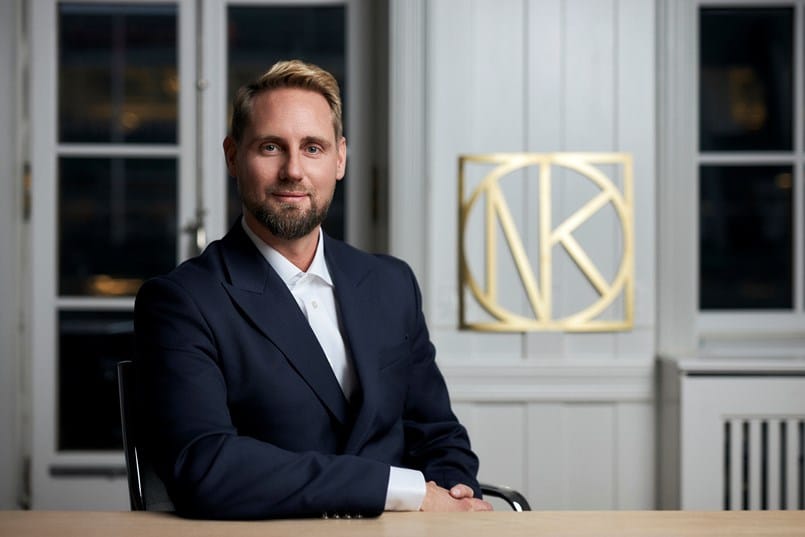 Man sitter vid bord framför NK-logotyp i kontor.