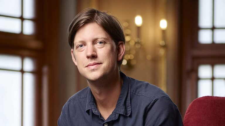 Man i svart skjorta ler mot kameran