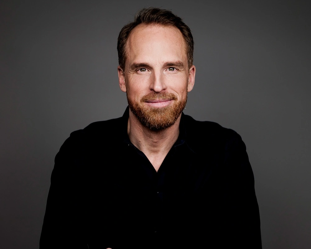 man i svart skjorta och skägg ler in mot kamerab