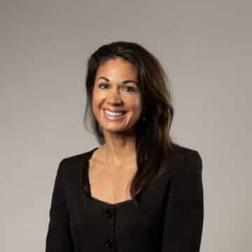 En kvinna med mörkt hår som ler mot kameran och har svart tröja på sig.