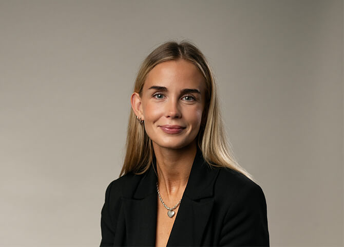Kvinna ler, sitter stilla, mot neutral bakgrund.