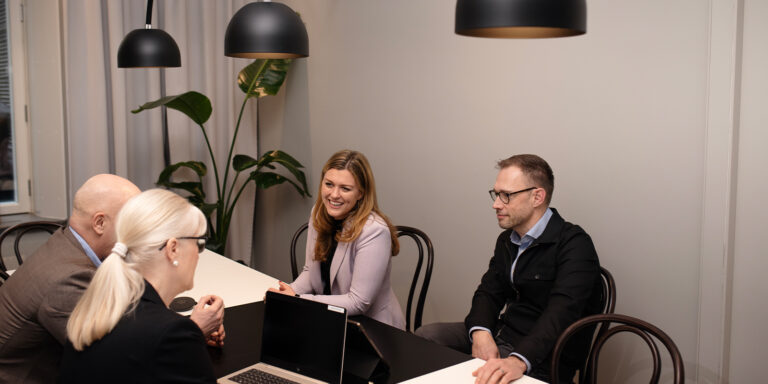 Fyra personer samtalar vid bord i modernt kontorsrum.
