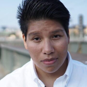 Person med kort hår blickar mot kameran utomhus.