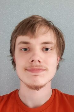 Person ler mot kameran, neutral bakgrund, orange tröja.