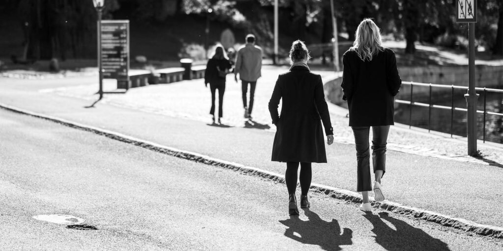 Personer promenerar på solig gångväg i parkområde.