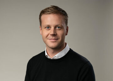 Person ler mot kameran, sitter framför neutral bakgrund. Inget text.