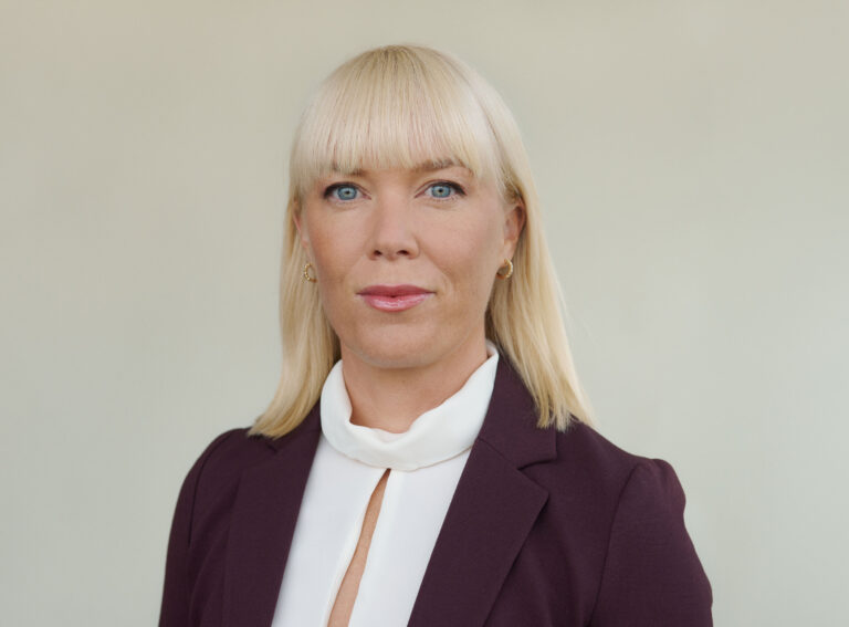 Kvinna med blont hår poserar i kostym framför bakgrund.