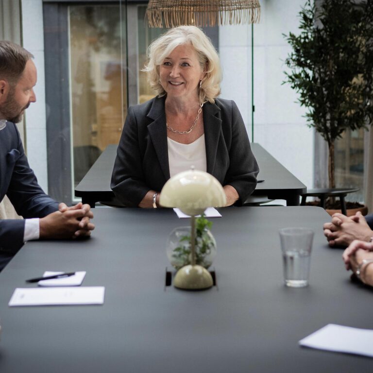 Kvinna leder möte vid bord, fyra personer deltar.