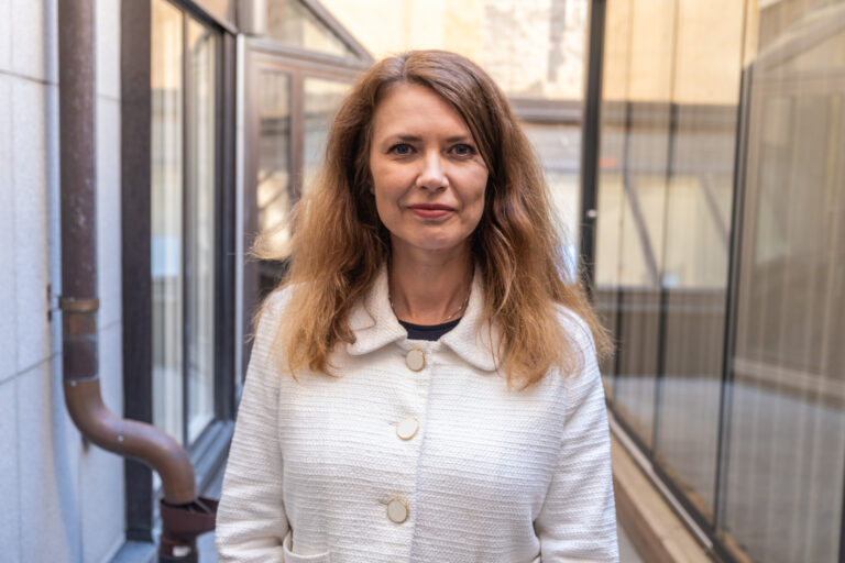 Kvinna står i en smal utomhuspassage mellan byggnader.