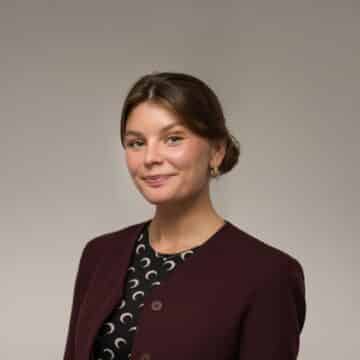 En Glad kvinna med håret i knut och vinröd kavaj.