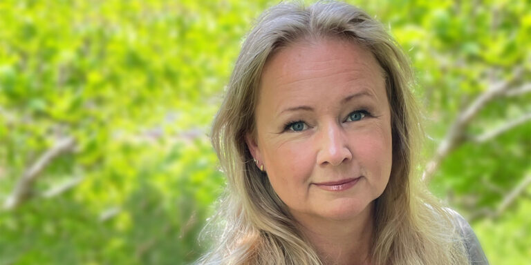 Kvinna står framför suddig grön bakgrund utomhus.