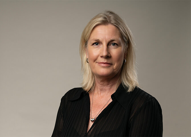 Kvinna ler mot kameran i en neutral bakgrund.