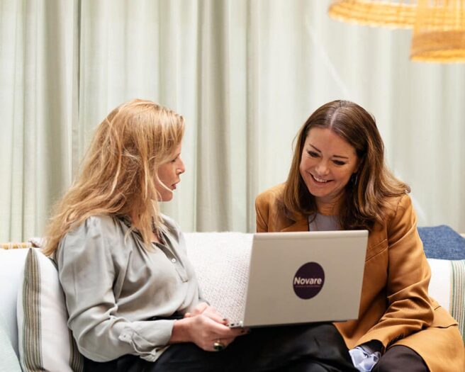 Två kvinnor som sitter och jobbar med laptops i en soffa.