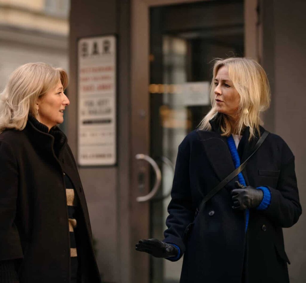 Två kvinnor samtalar utanför en byggnad på gatan.