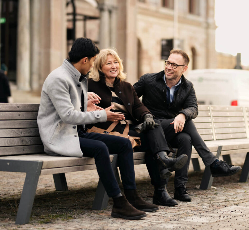 Tre personer samtalar på en bänk utomhus.