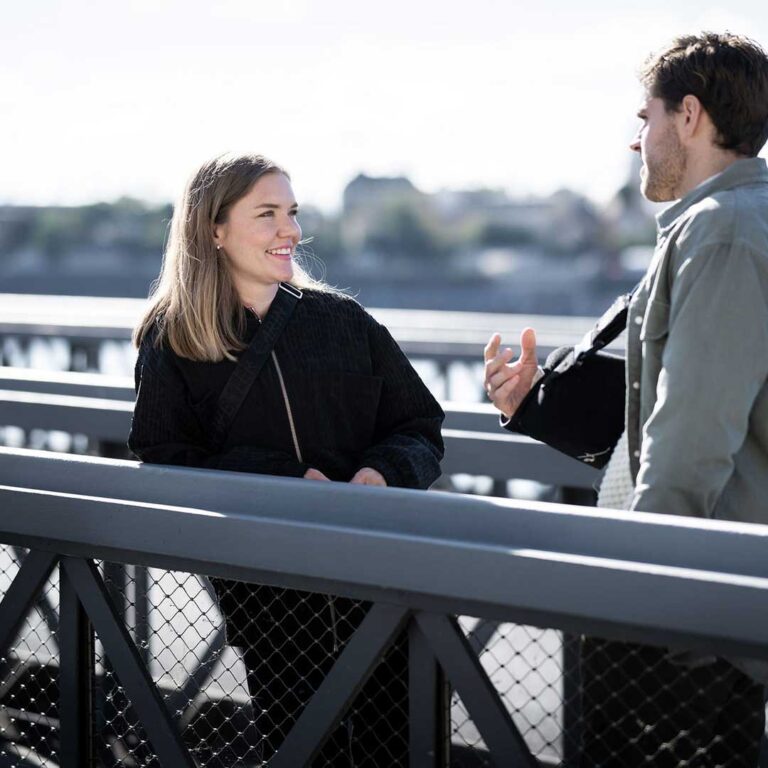 Två personer pratar och skrattar på en bro utomhus.