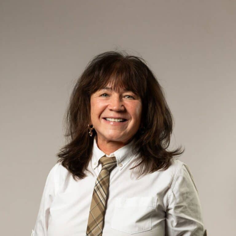 En glad kvinna som ler mot kameran med vit skjorta och slips