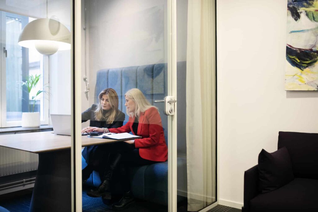 Två personer som sitter inne i ett kontorsbås och har ett möte.