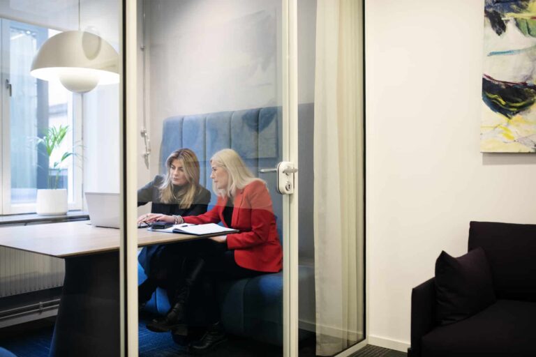 Två personer som sitter inne i ett kontorsbås och har ett möte.