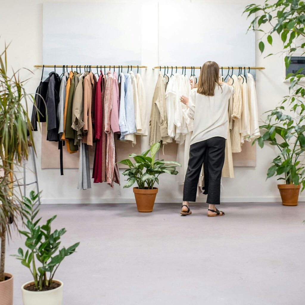 Kvinna som går och plockar vid kläder som hänger på en klädstång i butik.