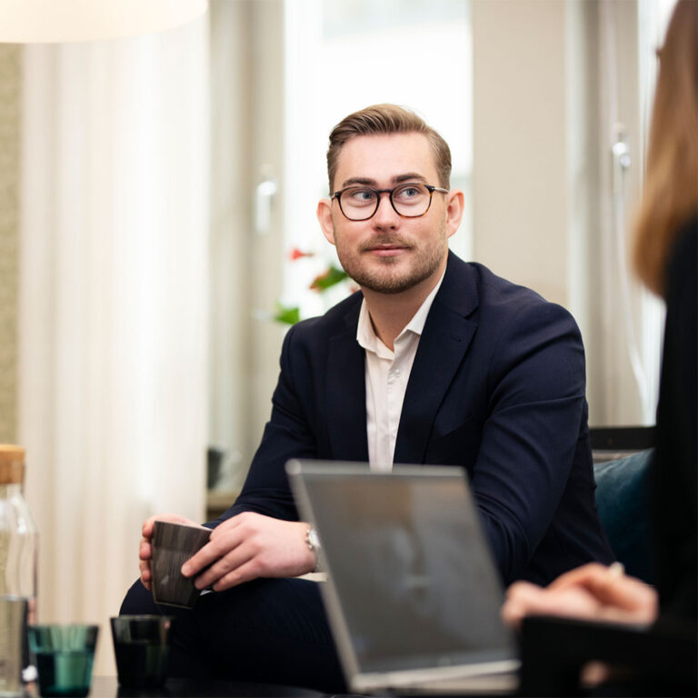 En sittande man tittar på en person som håller i en dator.