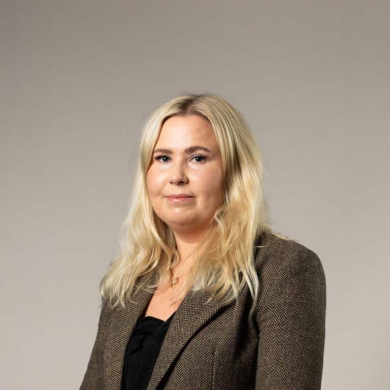 Blon leende kvinna med svart tröja och brun kavaj.