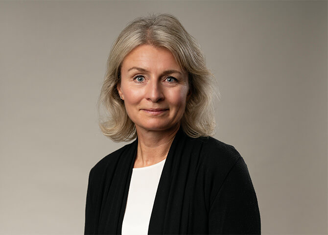 Kvinna med grått hår, tittar framåt mot lugn bakgrund.