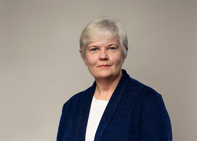 Kvinna står framför en grå bakgrund, bär blå kavaj.