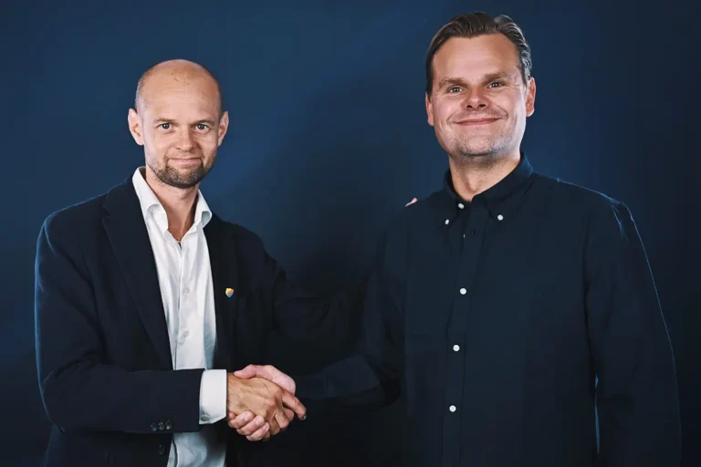 Två män som skakar hand och ler mot kameran