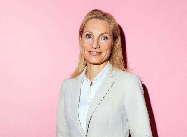 kvinna i ljus kostym ler in mot kameran. rosa bakgrund.