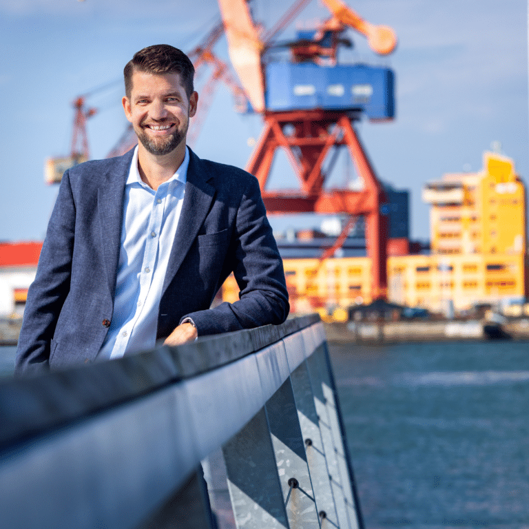 Man i blå kostym står med Göteborgs hamn i bakgrunden