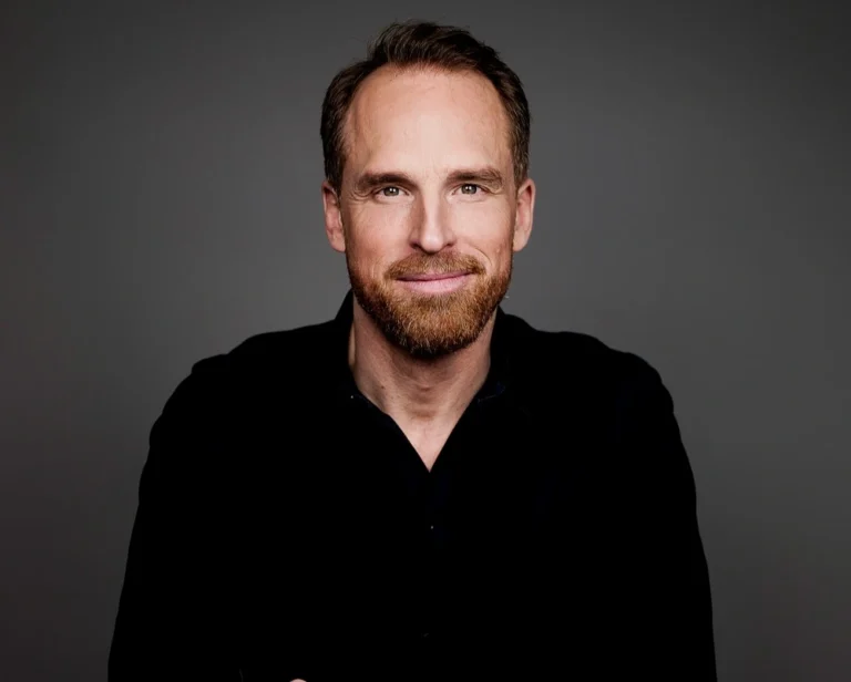 man i svart skjorta och skägg ler in mot kamerab