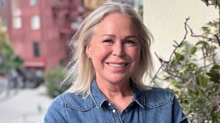 Kvinna i skjorta ler in mot kameran