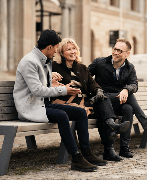 Tre personer samtalar på en parkbänk utomhus.